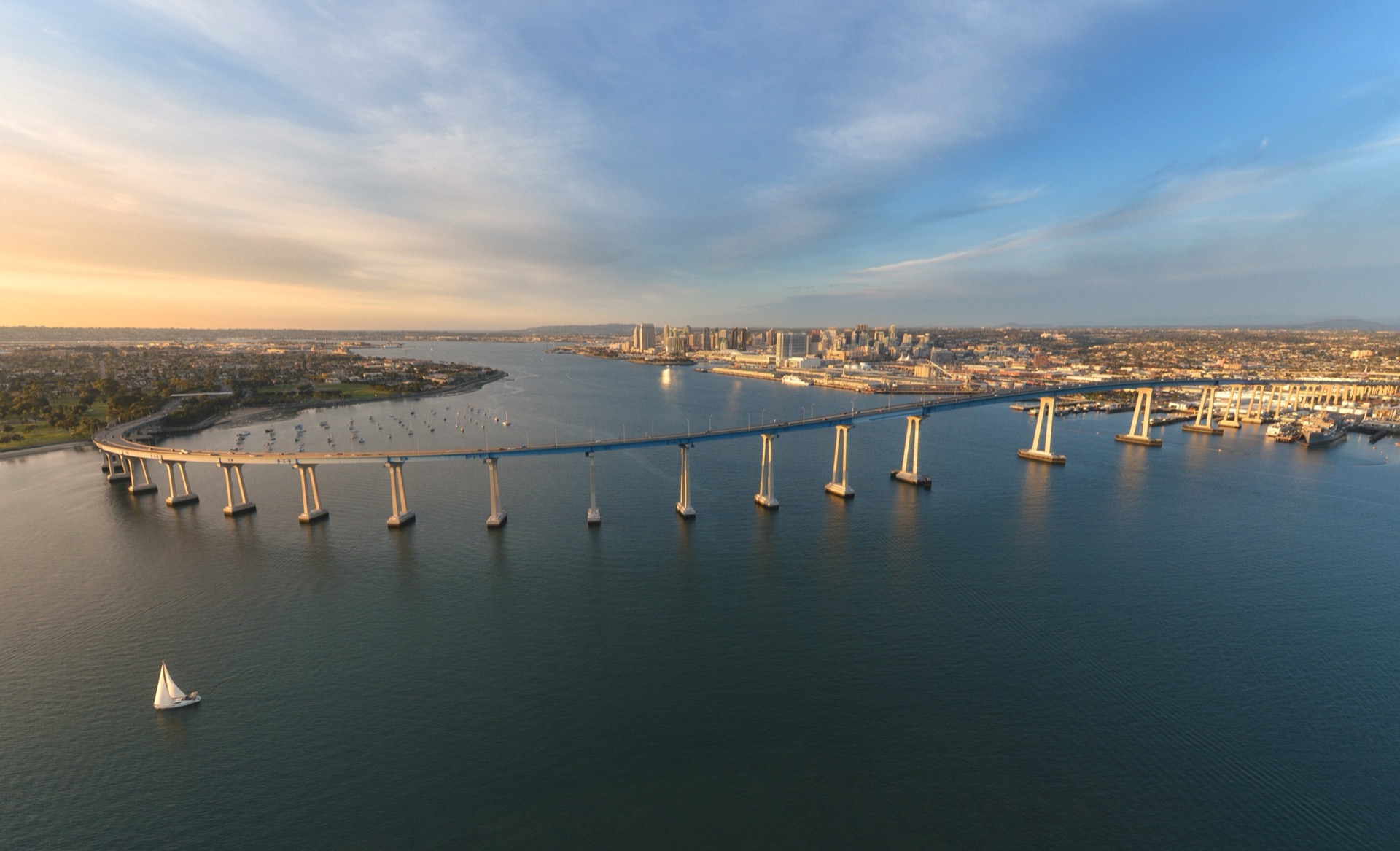 Aerial drone view of the San Diego-Coronado Bridge curving across the bay toward Coronado Island at golden hour